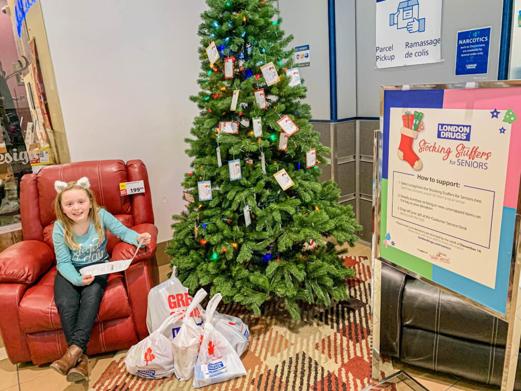 Child sitting in chair in front of Stocking Stuffers for Seniors tree at London Drugs