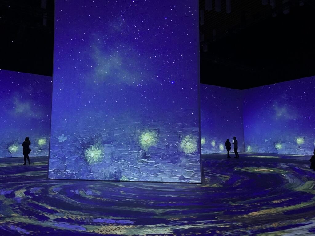 People silhouetted against Imagine Van Gogh projection screens
